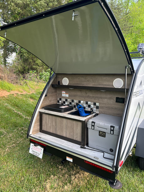 This RV rental features an open teardrop camper's rear kitchen with a sink, cooktop, and K2 cooler, ready for outdoor adventures.