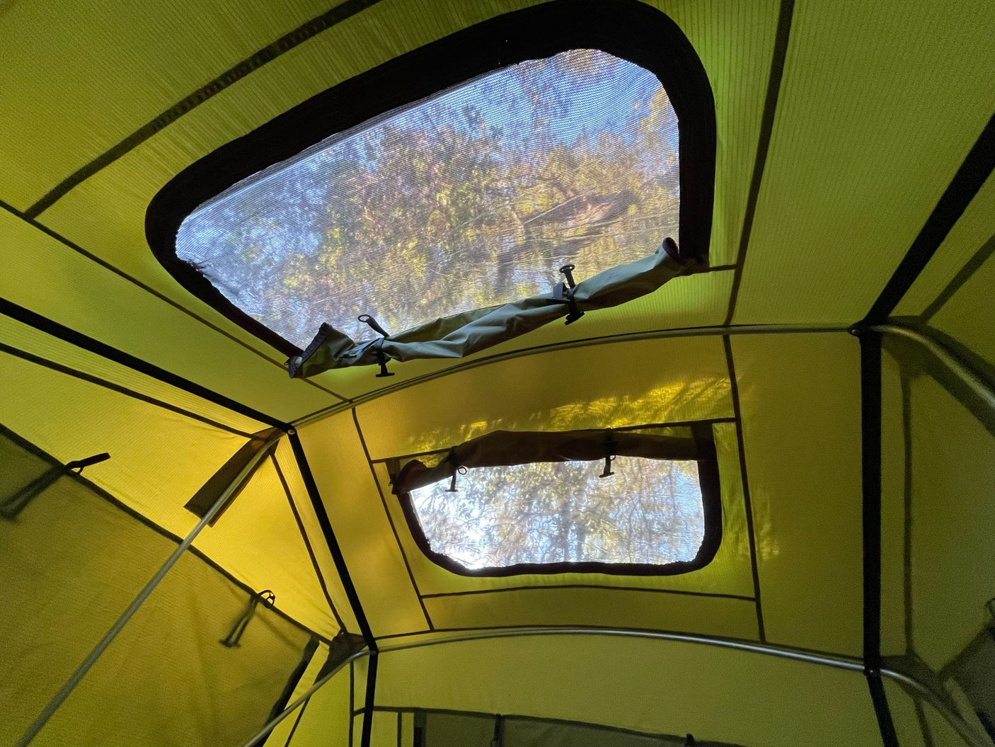 Interior view of a vibrant green RV rental roof tent with open mesh windows revealing bright trees & blue sky.