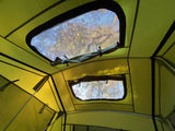 Interior view of a vibrant green RV rental roof tent with open mesh windows revealing bright trees & blue sky.