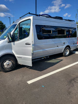 Silver Winnebago camper van, perfect for an RV rental, with its driver's door open in a parking lot.