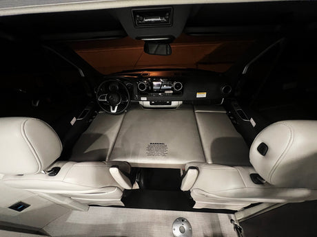 Inside an RV rental: front cabin with dashboard, steering wheel, and seats folded flat to form a bed.