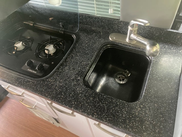RV rental compact kitchen: black speckled counter, two-burner stove, and sink with silver faucet. — photo 16