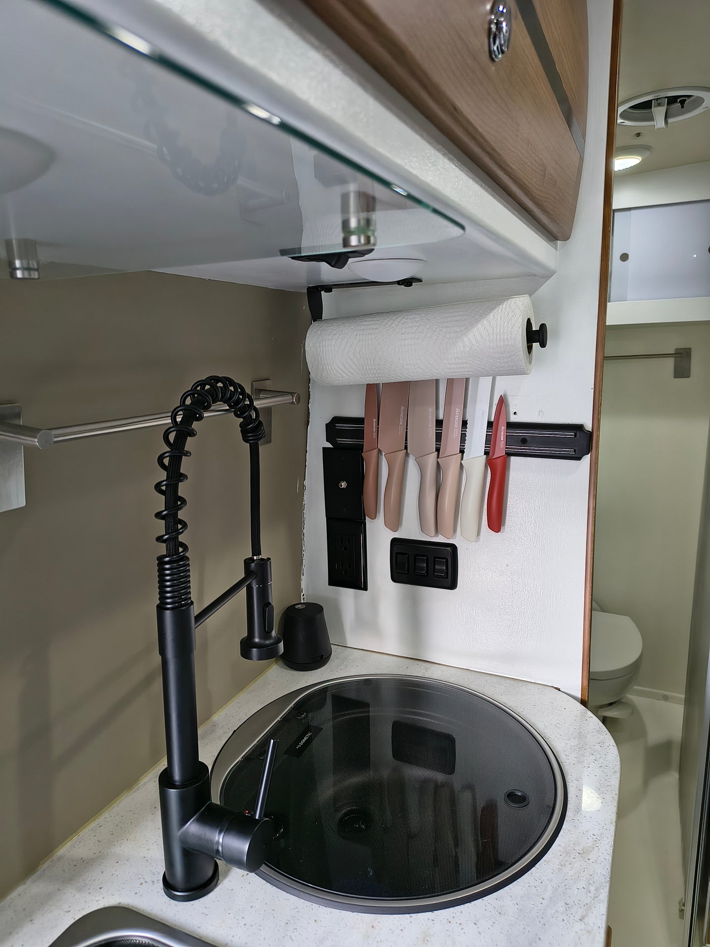 Compact RV rental kitchen featuring a modern black gooseneck faucet, covered sink/cooktop, and wall-mounted knife set.