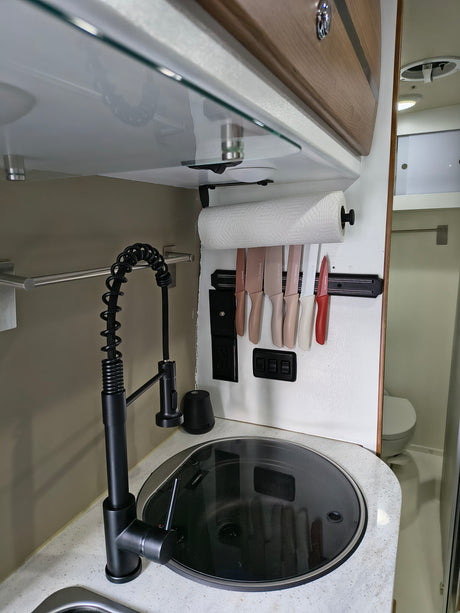 Compact RV rental kitchen featuring a modern black gooseneck faucet, covered sink/cooktop, and wall-mounted knife set.
