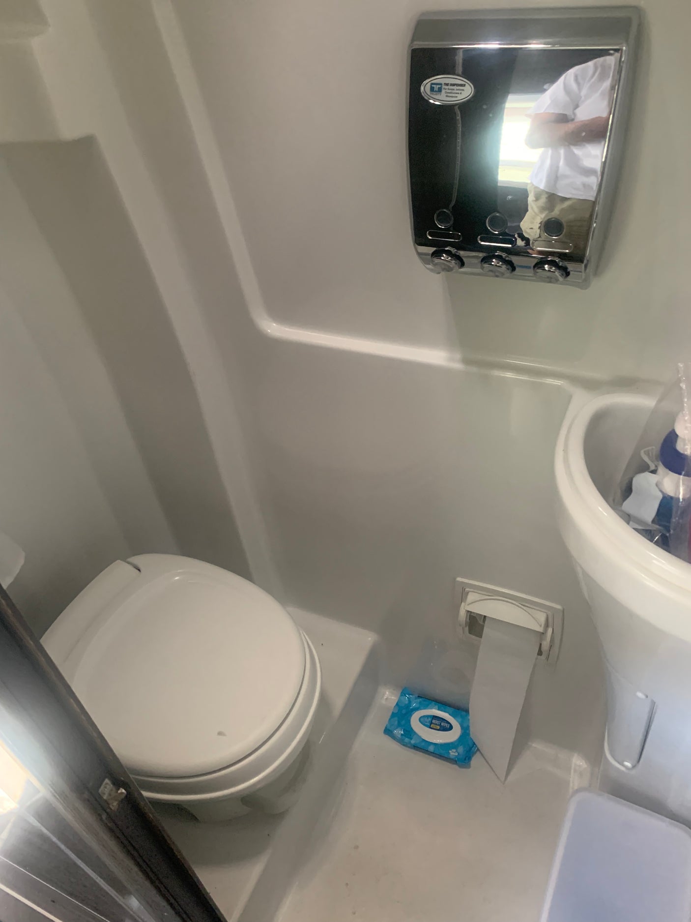 Compact RV rental bathroom with toilet, wall-mounted dispenser, and wet wipes, designed for travel convenience.