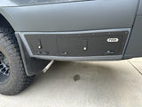 Modified RV rental van side with custom storage compartments and exhaust. Shows an off-road tire and concrete stain.