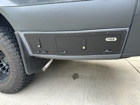 Modified RV rental van side with custom storage compartments and exhaust. Shows an off-road tire and concrete stain.