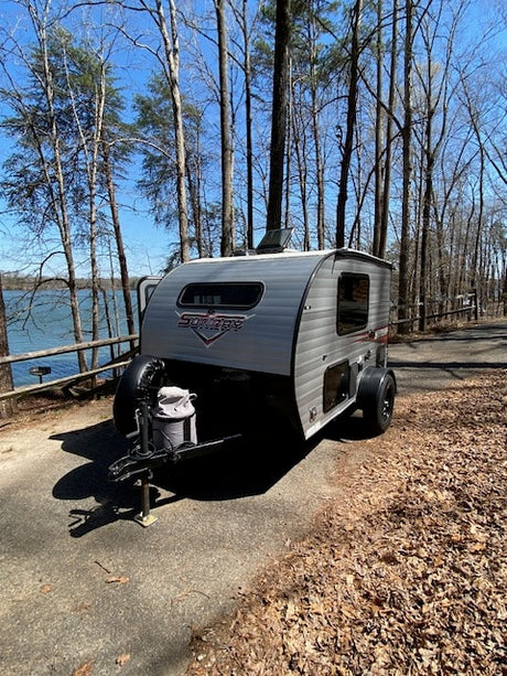 A compact RV rental is set up near a tranquil lake and trees, perfect for a peaceful camping getaway.