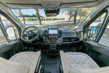 RV rental's modern cockpit, featuring a large touchscreen, steering wheel, and a scenic lake-mountain vista outside.