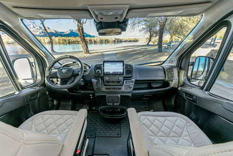 RV rental's modern cockpit, featuring a large touchscreen, steering wheel, and a scenic lake-mountain vista outside.