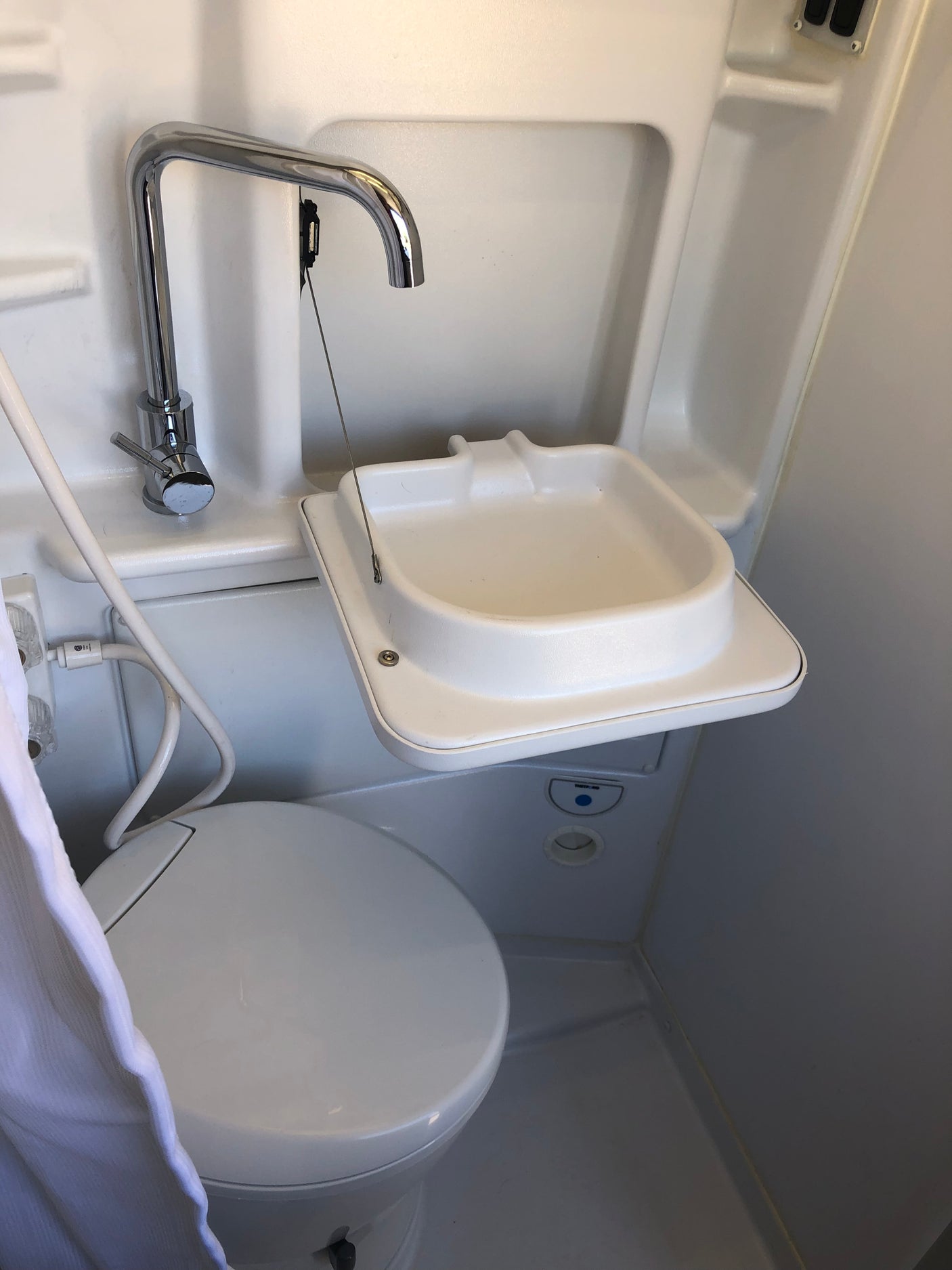 Compact RV rental wet bath with space-saving fold-down sink, toilet, and multi-use shower faucet.