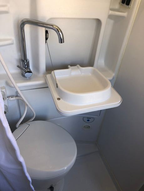 Compact RV rental wet bath with space-saving fold-down sink, toilet, and multi-use shower faucet.