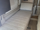 RV rental: Interior view of a functional sleeping/lounge area with patterned cushions, TV, and window blinds.