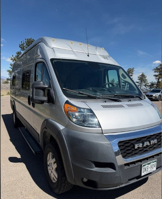 This silver Ram ProMaster rv rental, a camper van with a raised roof, is parked on asphalt under a blue sky, ready for adventure. — photo 7