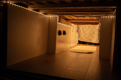 Functional RV rental under-bed storage area, illuminated by warm LED lights, with wooden floor and vents visible.