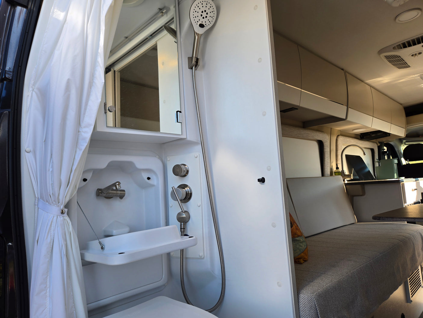 This RV rental features a compact bathroom with shower, sink, and mirror, alongside a cozy living area with seating and cabinets.