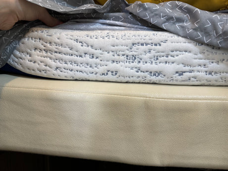 RV rental interior comfort: Hand holds grey patterned fabric above a white quilted blanket & cream seating cushion.