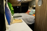 Cozy RV rental interior with a patterned bed, colorful pillows, and a compact kitchen area with a sink.