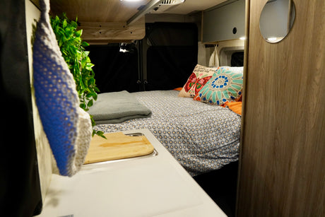 Cozy RV rental interior with a patterned bed, colorful pillows, and a compact kitchen area with a sink.