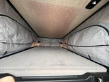 Inside an rv rental pop-up tent, showing a comfortable quilted mattress and grey fabric walls. Ideal sleeping area.