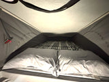Interior view of a cozy pop-top RV rental bed, featuring light pillows and a plaid blanket, ready for sleeping.
