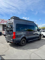 Dark gray Mercedes-Benz Sprinter RV, with a bike rack and awning, parked outdoors. Ideal for an rv rental adventure.