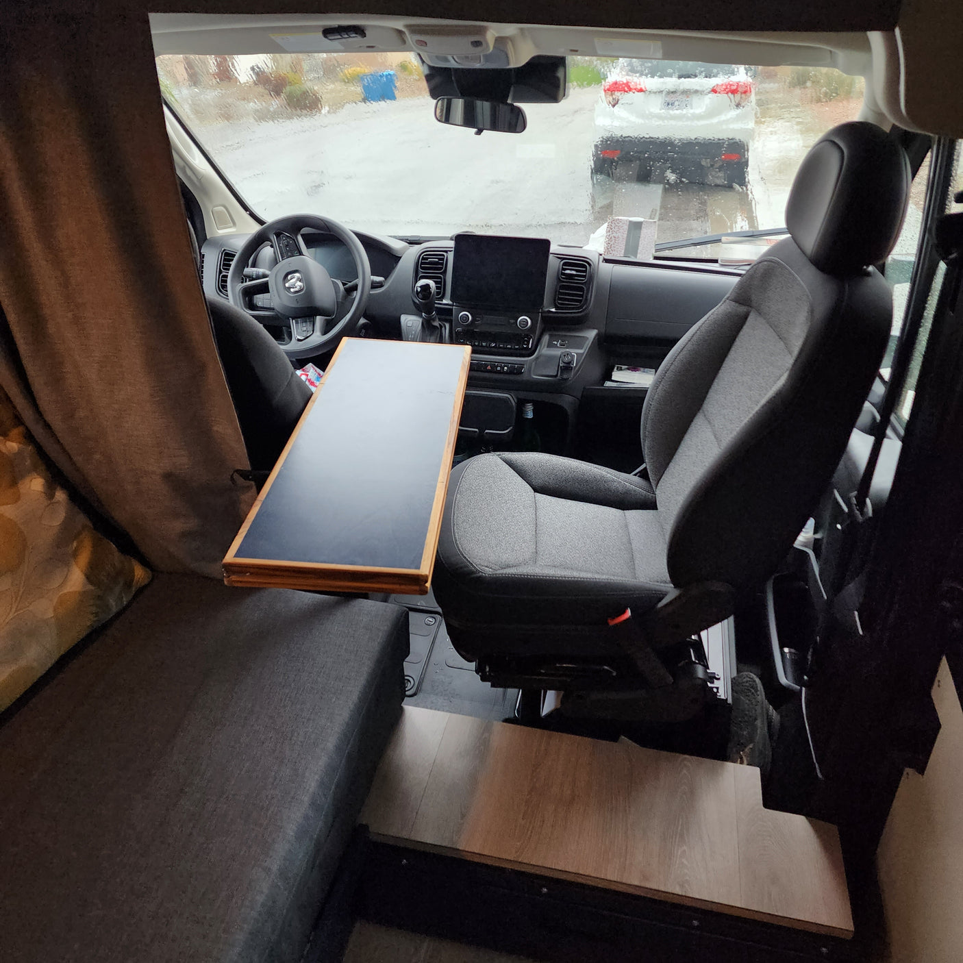 Interior of an rv rental, with the driver's cabin and a table visible. A rainy view can be seen through the windshield.