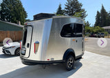 A sleek silver Airstream travel trailer (RV rental) sits on a driveway, ready for adventures. Perfect for glamping.