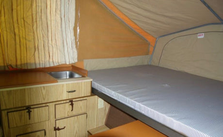 Interior of an RV rental pop-up camper: bed, small kitchen with sink, and wooden cabinets visible.