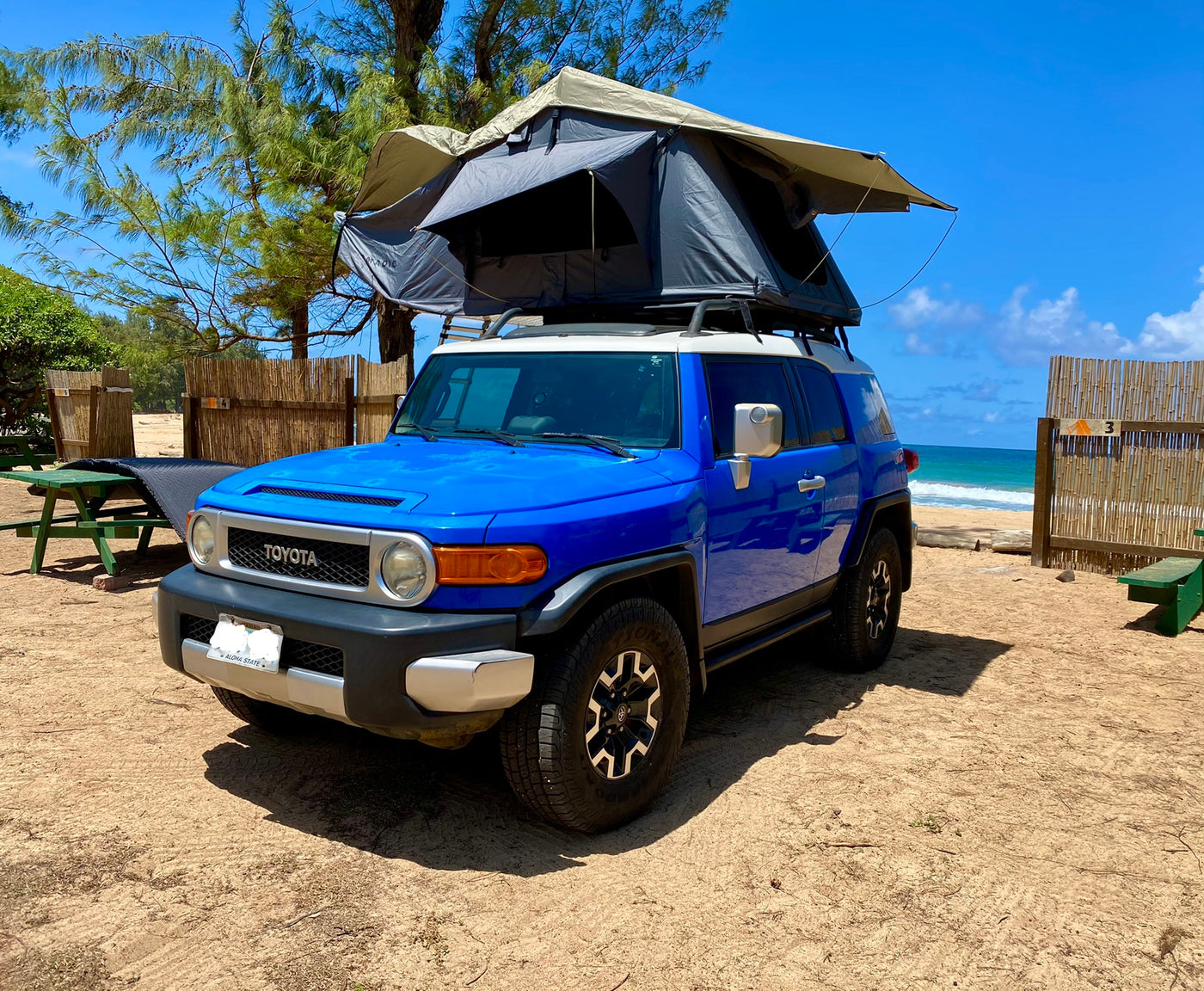 This RV rental is a blue Toyota FJ Cruiser with a rooftop tent, parked on a sandy beach by the ocean. — photo 5