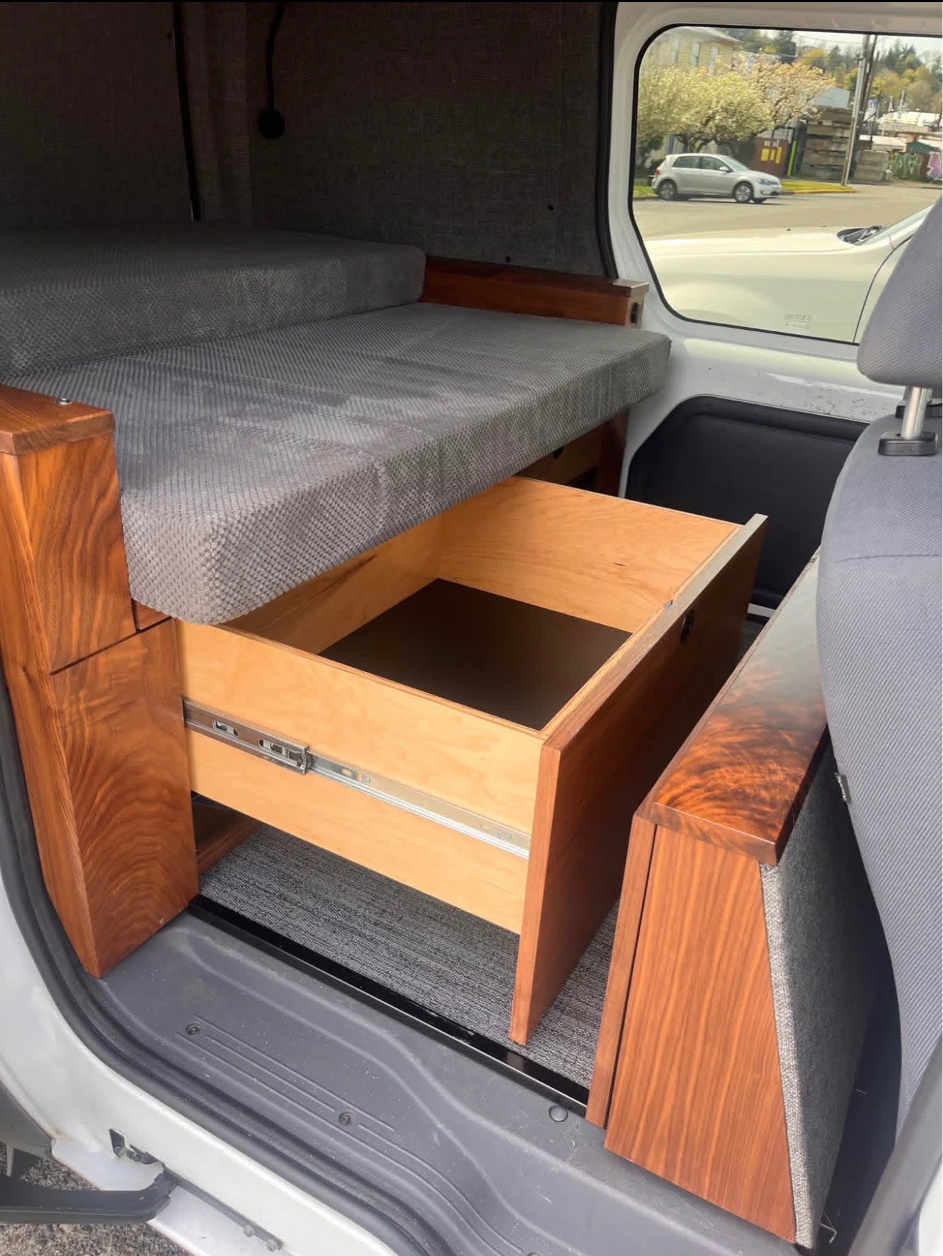  parked on concrete. Industrial building & cranes are in the background.|RV rental: Open drawer refrigerator with wire baskets in a modern camper van interior — photo 3