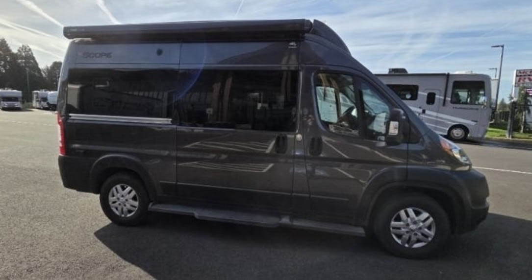 Dark gray Thor Scope Class B RV rental, a compact camper van, parked in a lot with other motorhomes.