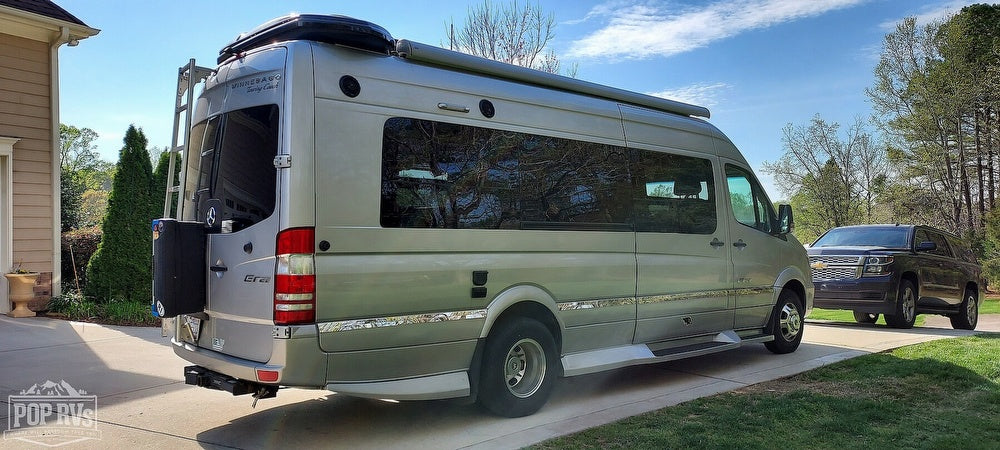 This light grey Winnebago Era RV rental, a compact camper van, is parked outside a house on a sunny day.