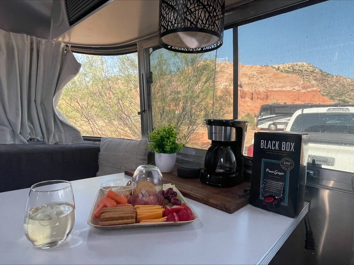 Enjoying an RV rental: a cozy setup with wine, coffee, snacks, and a stunning desert mountain view, including other RVs.