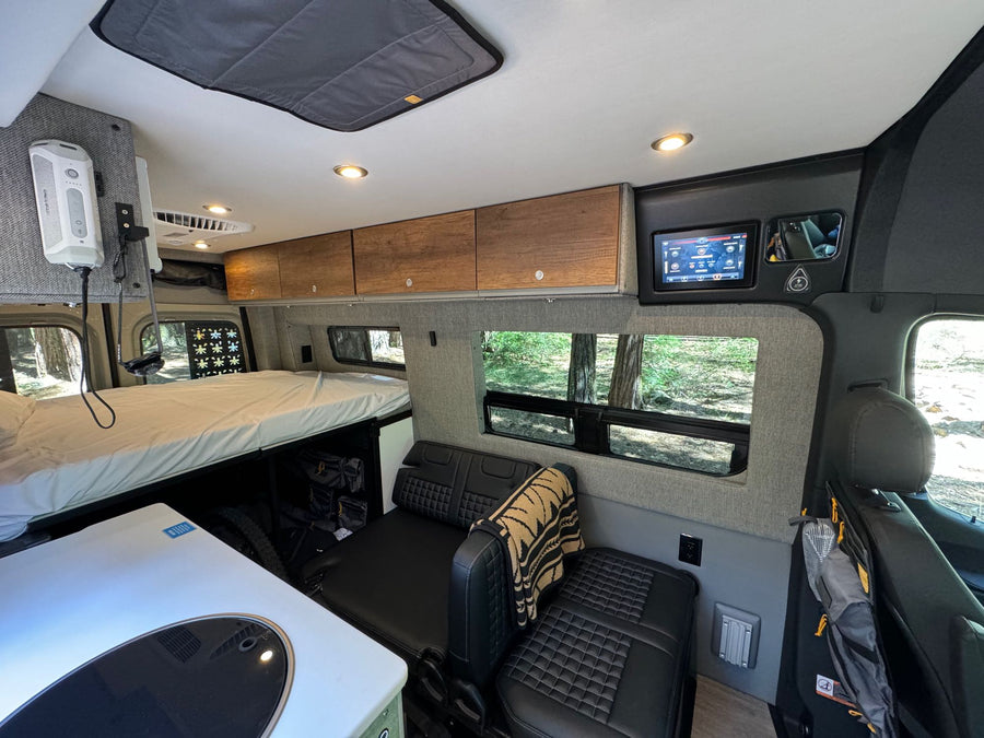 Modern RV rental interior with elevated bed, compact kitchen, and lounge seating, perfect for a comfortable road trip.