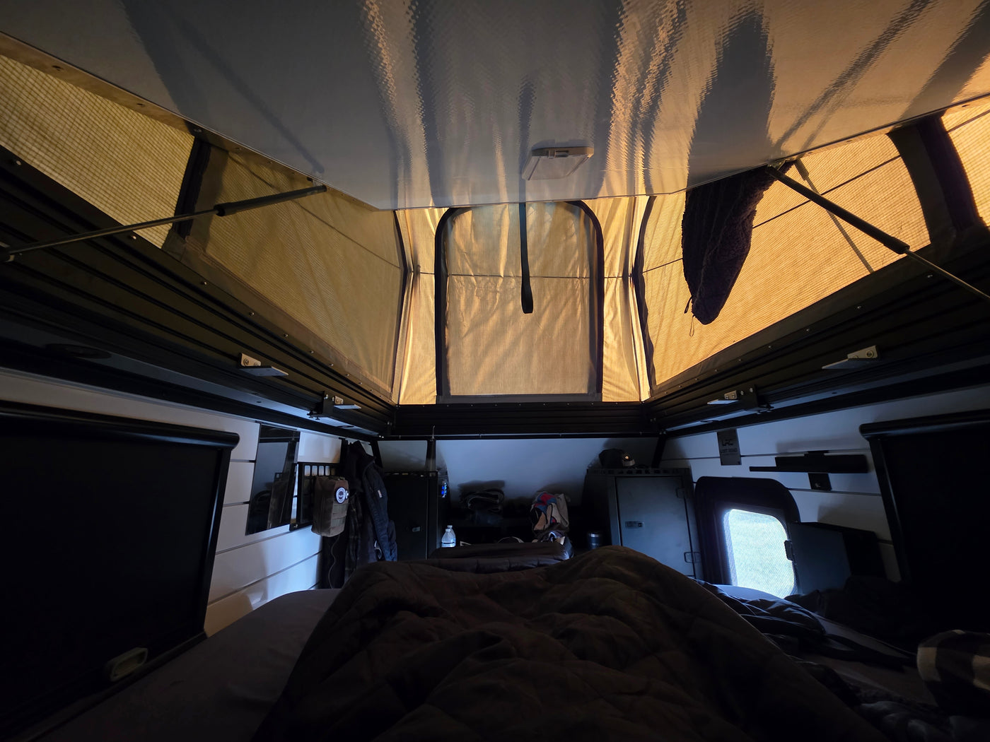 Inside an RV rental pop-top camper, a cozy sleeping area and storage are visible below the mesh windows and high ceiling. — photo 8
