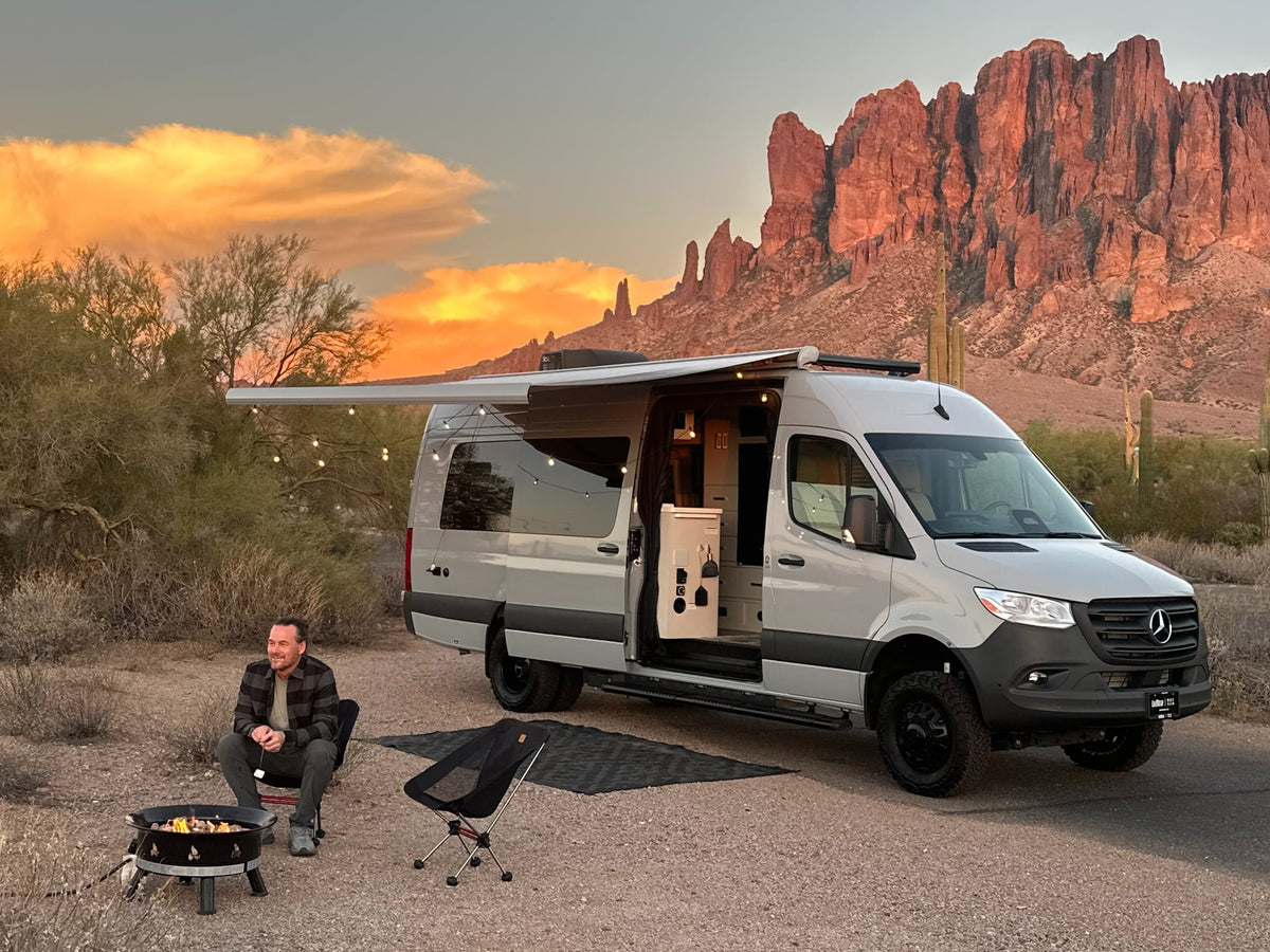 Desert sunset camping with an RV rental. Man roasts marshmallows by campfire near a Mercedes Sprinter van.|Grey Sprinter RV rental camper van with off-road tires parked by a road