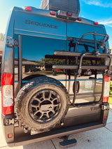 Rear of a dark gray Thor Sequence RV, with spare tire and gear rack, featuring an Outdoorsy sticker for RV rental.