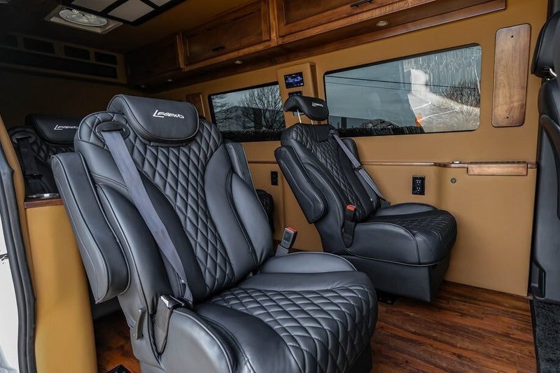 Plush RV rental interior features black diamond-stitched captain's chairs with "Legends" headrests, wood cabinets, and flooring. — photo 11