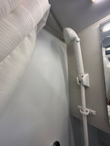 Inside an RV rental: a white handheld shower with hose, mounted on a textured wall, next to a patterned shower curtain.