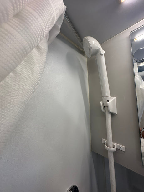Inside an RV rental: a white handheld shower with hose, mounted on a textured wall, next to a patterned shower curtain.