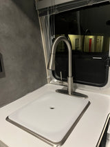 Modern RV rental kitchen featuring a sleek stainless steel faucet, white countertop, and sink cover.