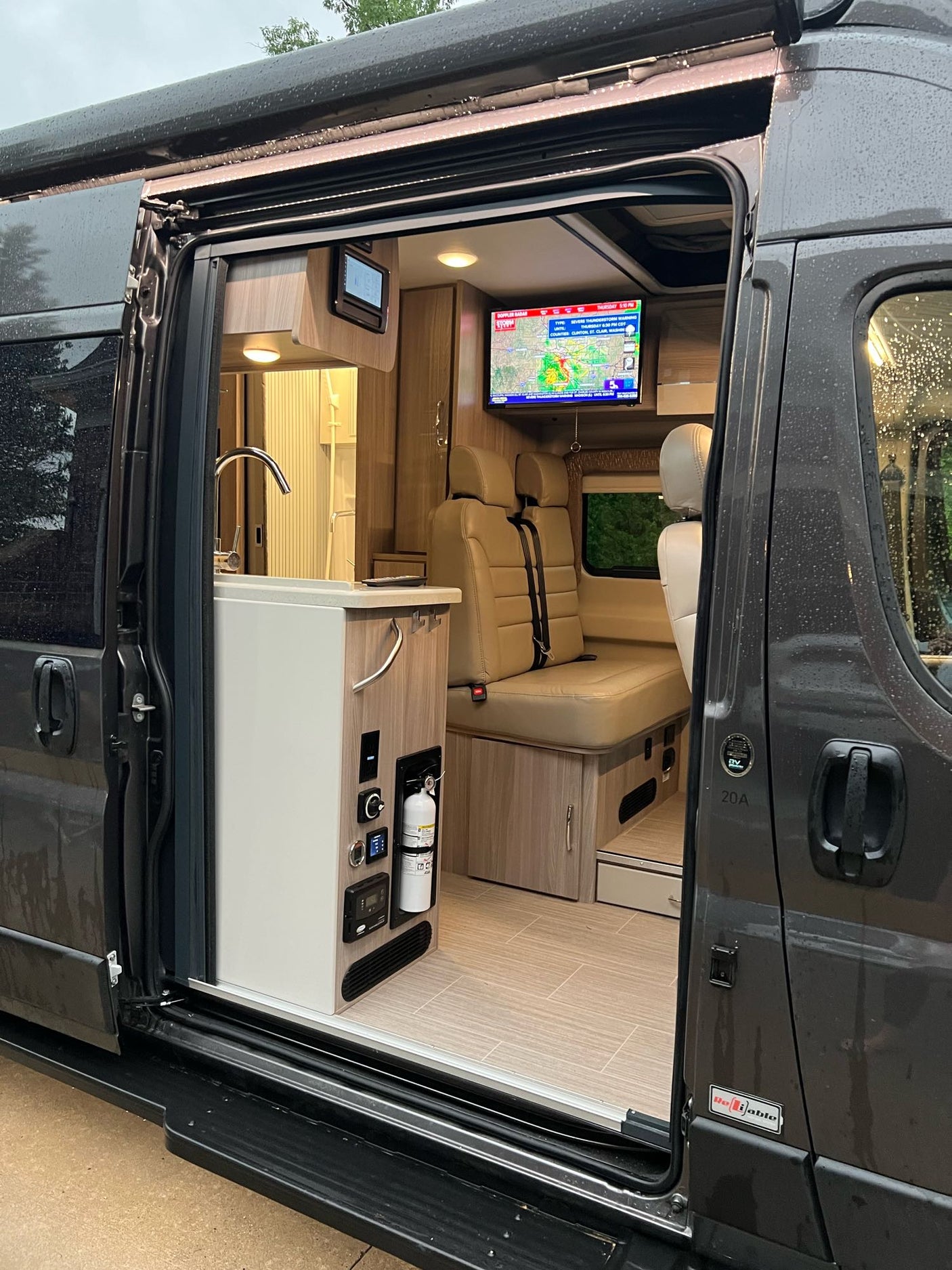 Step into this modern RV rental camper van! The open door reveals a sleek kitchen, cozy seating area, and TV inside.