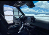RV rental cabin view: Steering wheel, dashboard, and snowy mountains through the open van door.