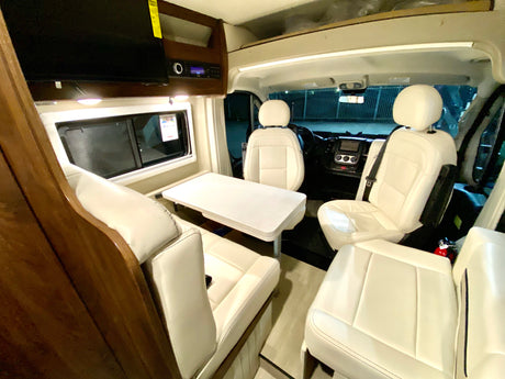 Spacious RV rental interior with white leather seating, a dining table, and a view of the driver's cockpit.