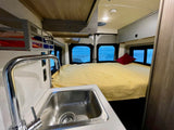 Cozy RV rental interior featuring a bed, kitchen sink, and stunning ocean views. Perfect for your next adventure!