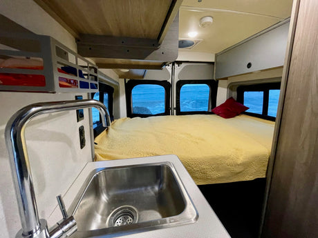 Cozy RV rental interior featuring a bed, kitchen sink, and stunning ocean views. Perfect for your next adventure!