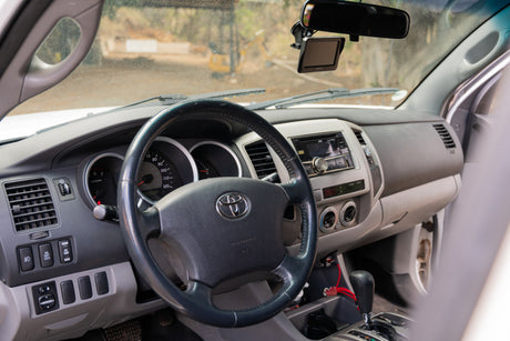Dashboard and driver's view inside a Toyota truck, showing steering wheel, stereo, and dusty windshield. Ideal for an RV rental.