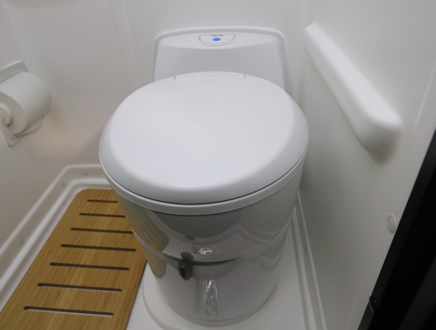 Compact RV rental wet bath featuring a white cassette toilet, toilet paper holder, and slatted wooden floor mat. — photo 16
