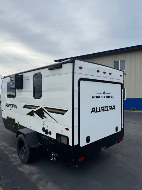 A white Forest River Aurora camper trailer, ideal for your next rv rental adventure. Features black trim, windows, and rugged wheels.